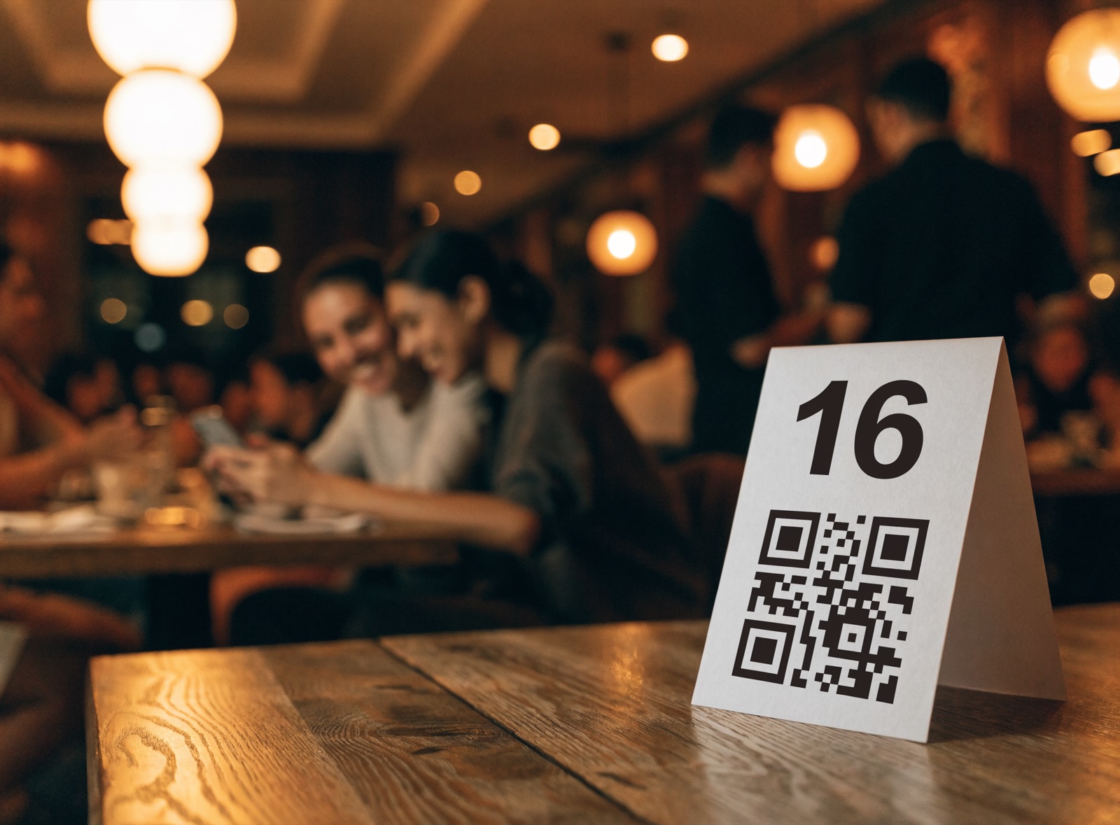 Cartão de QR com o número da mesa em cima da mesa, e o salão cheio ao fundo